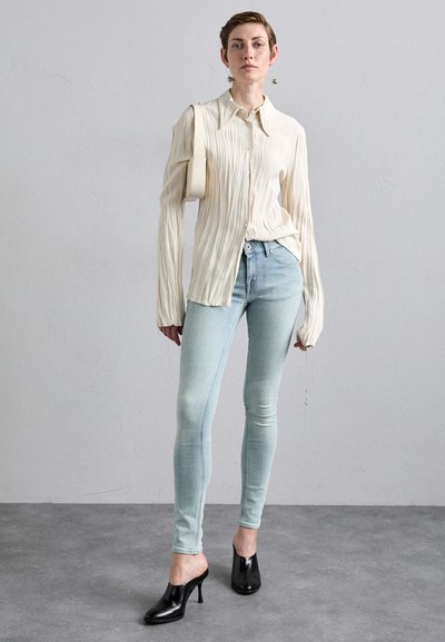 Rynket elfenbensfarget langermet skjorte, lyseblå skinny jeans og svarte hæl mules. Minimalistisk design med subtile teksturer og rene linjer.