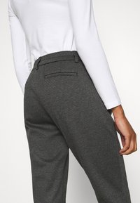 Grijze, gestructureerde broek met een getailleerde pasvorm, achterzakken en een tailleband. Gemaakt in combinatie met een witte lange mouwen top.