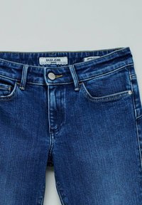 Jeans de denim azul oscuro con un diseño recortado, que cuentan con costuras claras, un cierre frontal con botón y un pequeño bolsillo en el lado derecho.