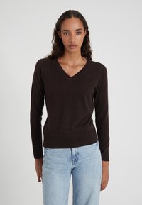 Brauner V-Ausschnitt-Pullover aus weichem Material, mit langen Ärmeln und geripptem Saum. Kombiniert mit hellblauen Jeans für einen lässigen Look.