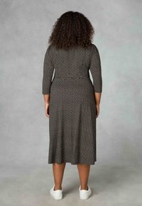 Ruskea kuviollinen mekko, jossa on kolmivartiset hihat, keskipitkä pituus, istuva vyötärö ja laineileva hame, yhdistettynä valkoisiin lenkkareihin.