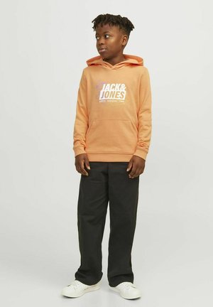 Oranges Kapuzen-Sweatshirt mit weißem Grafiklogo, Vorderentasche und gerippten Bündchen. Kombiniert mit schwarzen Hosen und weißen Sneakern.