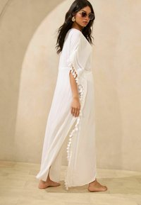 Weißes Maxikleid mit Quastenakzenten und kunstvollen Details an den Ärmeln, aus leichtem Stoff, fließendes Design, knöchellang.