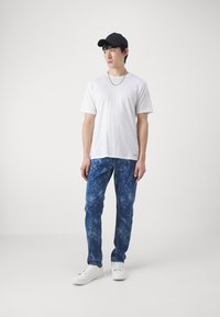 Hvit t-skjorte med korte ermer, blå tie-dye jeans, hvite sneakers og en svart caps. Enkelt design, bomullstoff, avslappet passform og subtil tekstur.