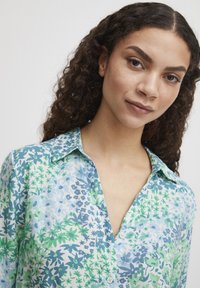 Cămașă cu butoni florală în nuanțe de albastru deschis și verde, având un guler, modele mixte de flori și frunze, și o textură de țesătură moale și netedă.