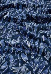 Granatowa tkanina z powtarzającym się wzorem jasno-niebieskich i białych abstrakcyjnych kształtów wodorostów, o teksturowanym, falistym wyglądzie.