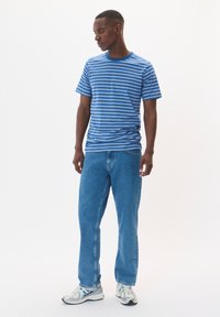 Mėlynos dryžuotos marškinėliai su apvaliu iškirpimu, derinami su šviesiai mėlynomis tiesiomis kelnėmis ir pilkais sportbačiais su mėlynais akcentais.