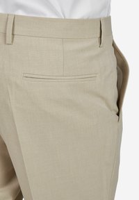 Beige op maat gemaakte broek van lichtgewicht stof. Kenmerkt zich door een vlakke voorkant, zijzak en achterste paspelzak met subtiele stikdetails.