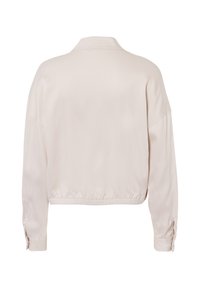 Lichtbeige cropped jacket met een gladde satijnen afwerking, mandarin kraag en elastische zoom. Heeft lange, iets wijde mouwen met knoopmanchetten.