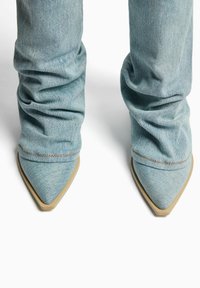 Helle blaue Denim-Stiefel mit lässigem Design, spitz zulaufender Zehenpartie und beigem Fußbett. Sichtbare Nähte entlang der Kante.