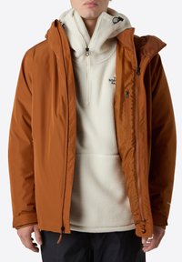 Chaqueta impermeable naranja para hombre con bolsillos con cremallera, superpuesta a un pulóver de forro polar crema con diseño de media cremallera y logo bordado.