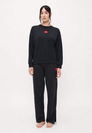 Zwart sweatshirt en broekset gemaakt van gladde stof. Het sweatshirt heeft een rood logo-patch; de broek heeft zij-splitten en een bijpassend logo.
