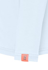 Lichtblauw langharig T-shirt van zachte stof, met een koraal kleurig label met een hondenafdruk vlakbij de zoom, en een afgeronde manchetontwerp.