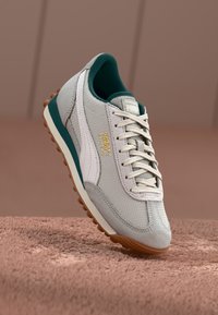 Szürke textil és velúr sneaker fehér részletekkel, zöld elemekkel, arany logóval és barna gumitalppal. Hagyományos fűzőzárral rendelkezik.