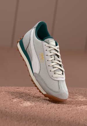 Sneaker in tessuto grigio e suede con accenti bianchi, dettagli verdi, logo dorato e suola in gomma marrone. Presenta una chiusura con lacci tradizionale.