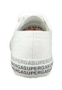 Białe trampki z płótna o fakturowanym wykończeniu, z markową gumową podeszwą z powtarzającym się napisem "SUPERGA" w granatowym kolorze. Okrągły tył.