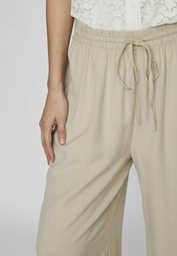 Pantalons légers beige clair, amples, avec une taille élastique et un cordon de serrage. Le tissu semble doux avec une texture lisse et une coupe droite.