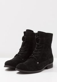 Stivaletti in suede nera fino alla caviglia con punta arrotondata, chiusura a lacci frontale, zip laterale e tacco basso a blocco. Presentano una texture morbida e leggere accentuazioni hardware.