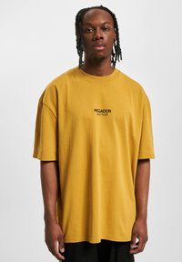 Senne gul oversized t-skjorte laget av bomull, med rund hals og svart tekstdetalj "PEGADOR BUILT TO LAST" på fronten.