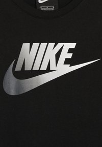 Černé bavlněné tričko s velkým kovovým stříbrným logem Nike a zakřiveným designem swoosh uprostřed.