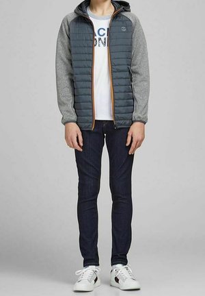 Polstret grå jakke med hætte, der har en ensfarvet krop og grå ærmer, parret med mørke jeans og hvide sneakers.