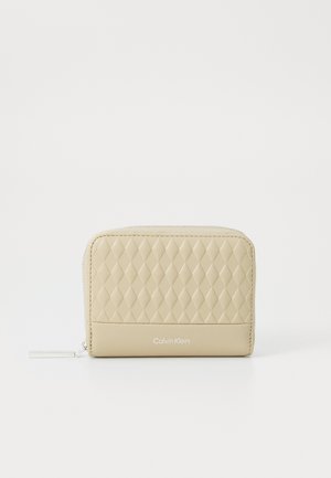 Portafoglio in faux leather trapuntato beige con una sezione inferiore liscia, chiusura zip e un branding sottile sulla parte frontale. Pattern a diamante testurizzato nella parte superiore.