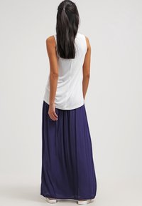 Top blanco sin mangas con escote redondo, combinado con una larga y fluida falda maxi morada. Tela suave con un corte relajado.