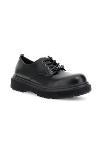 Scarpa in pelle nera con lacci, suola spessa e scanalata, e aghi metallici sui lacci, inclinata leggermente a destra su uno sfondo bianco.