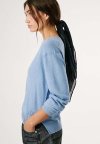 Šviesiai mėlynas megztinis su ilgomis rankovėmis ir raukšlėtu apvadu, derinamas su juoda šaliku, surištu gale, dėvimas ant tamsių džinsų.