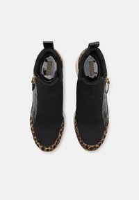 Scarpe slip-on nere in maglia con un accento leopardato lungo la suola, dettagli in pelle nera liscia e una piccola cerniera laterale.