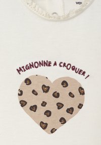 Kremfarbene Baumwoll-T-Shirts mit einem Spitzenbesatz am Ausschnitt; zeigt ein braunes Leopardenherz und burgunderfarbene Schrift "Mignonne à croquer !" darüber.