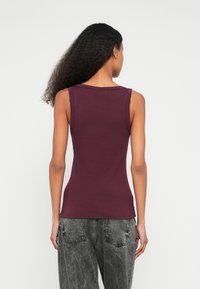 Viininpunainen hihaton paita, jossa pyöreä pääntie, istuva malli ja sileä pinta, yhdistettynä harmaisiin, väljälahkeisiin happopesu farkkuihin.