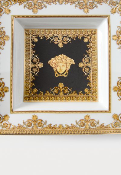 Štvorcový porcelánový tanier s čiernym stredom zdobeným zlatým motívom Medúzy, obklopený zložitými zlatými vzormi a rámami.