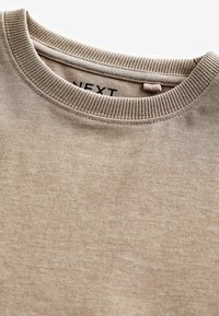 Ljus beige rundhalsad tröja i mjukt material med ribbat krage och nederkant, med en liten märkesetikett inuti.