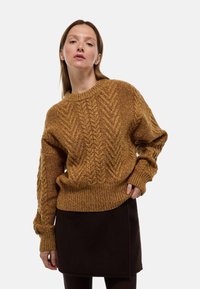 Pull en maille torsadée moutarde avec un col rond et des poignets côtelés, associé à une jupe marron foncé. Texture douce, coupe ample et motif détaillé.