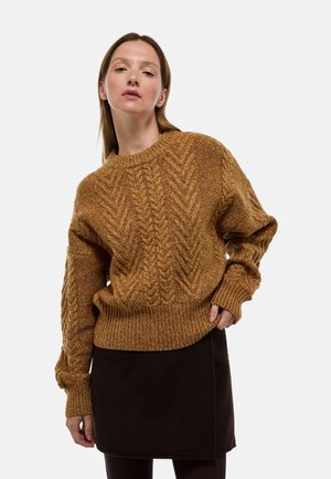 Pull en maille torsadée moutarde avec un col rond et des poignets côtelés, associé à une jupe marron foncé. Texture douce, coupe ample et motif détaillé.