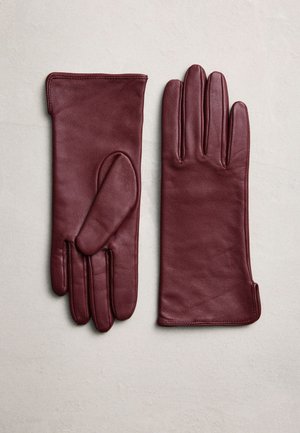 Un par de guantes de cuero color burdeos dispuestos sobre una superficie clara, uno con la palma hacia arriba y el otro con el dorso hacia arriba.