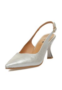 Zapato de tacón alto plateado tipo slingback con punta afilada, acabado de cuero metálico suave y tacón curvado. Plantilla marrón visible.