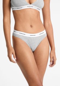 Szare bawełniane majtki elastyczne z białą, elastyczną tasiemką z czarnym logo "GUESS JEANS". Prosty, bezszwowy design, styl tanga.