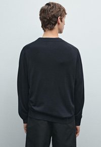 Černý pletený svetr s dlouhými rukávy a kulatým výstřihem, který má volnější střih a žebrovaný lem. Hladká textura a minimalistický design.