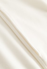 Weißer Baumwollstoff mit glatter Textur, der entlang des Randes eine subtile Nahtdetail aufweist. Die Oberfläche wirkt weich und sauber.
