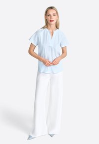 Blusa a righe blu e bianche con maniche corte, scollatura a V e vestibilità ampia, abbinata a pantaloni bianchi a gamba larga e scarpe blu con punta.