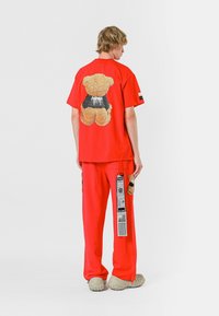 Conjunto de camiseta y pantalones rojos, con un gráfico de oso de peluche en la parte posterior. Tejido suave, corte relajado, con un detalle de etiqueta en los pantalones.
