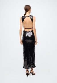 Black sequin dress with an open back, fitted silhouette, and knee-length design. Features a small strap and mid-thigh slit at the back.