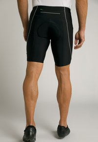 Shorts de cyclisme noirs en matériau extensible, avec un coussin rembourré rond, des accents réfléchissants et une petite poche zippée à l'arrière.