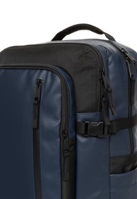 Marineblauwe rugzak van duurzaam materiaal, met zwarte gaasaccenten, meerdere ritsvakken en een handvat aan de bovenkant voor gemakkelijk dragen.