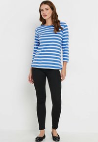 Gestreiftes langärmliges Oberteil in Blau und Weiß aus weichem Stoff; kombiniert mit schwarzen Slim-Fit-Hosen und schwarzen Ballerinas.