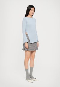 Light blue ribbed sweater with flared sleeves, paired with a black and white checkered mini skirt. Gray socks and pointed white shoes complete the look.