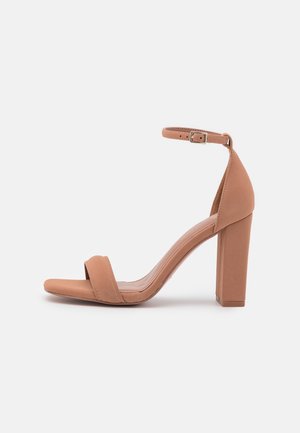 Sandale à talon haut de couleur fauve avec talon bloc, bride à la cheville avec boucle et une seule bride avant sur les orteils sur fond blanc.