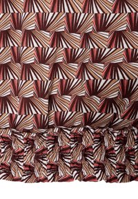 Bruin, wit en rood gestippeld stof met geometrische vormen, met een rucheszoom. De textuur lijkt zacht en iets elastisch.
